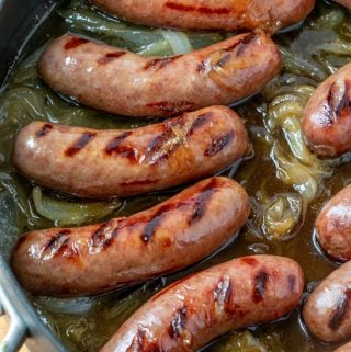 Overhead of grilled brats in saute pan with reduced beer and tender onions