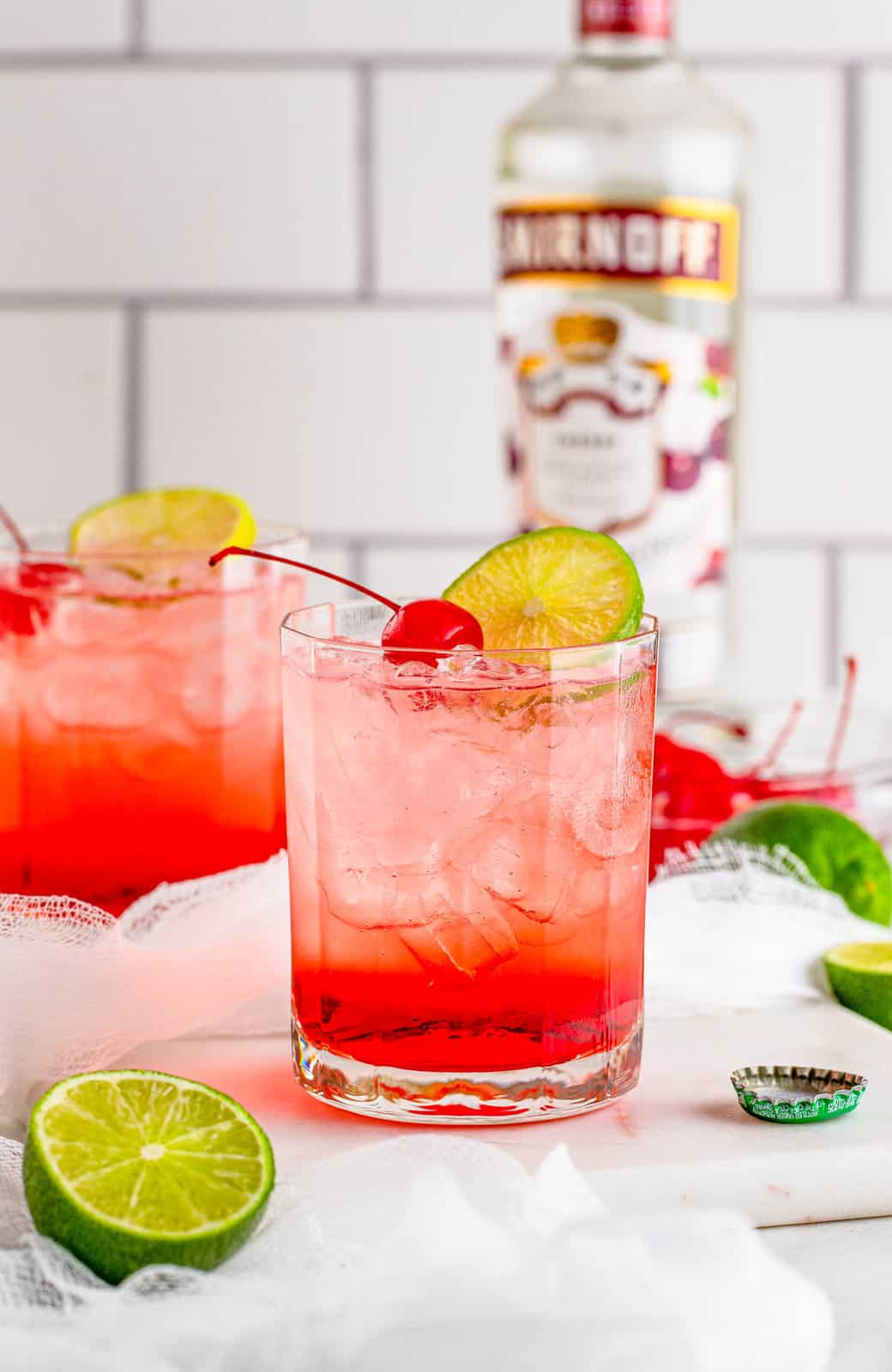 Two Dirty Shirleys on marble board with alcohol in background.